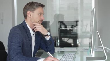 Düşünceli iş adamı stratejik planlamaya odaklanmış, modern ofis ortamında bilgisayar ve evrak işleriyle masa başında notlar yazıyor. İş adamları konsepti