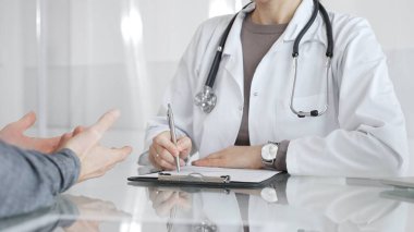 Klinikteki hasta muayenesi sırasında panoya not alan beyaz önlüklü doktor sağlık, teşhis ve bakım kararlarına odaklanmış. İlaç ve sağlık hizmetleri