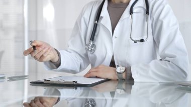 Panoya yazı yazan, steteskop takan, ilaç, sağlık, teşhis ve tedavi kavramlarını yansıtan beyaz önlüklü bir doktor. İlaç ve sağlık hizmetleri