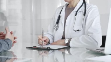 Klinikteki hasta muayenesi sırasında panoya not alan beyaz önlüklü doktor sağlık, teşhis ve bakım kararlarına odaklanmış. İlaç ve sağlık hizmetleri