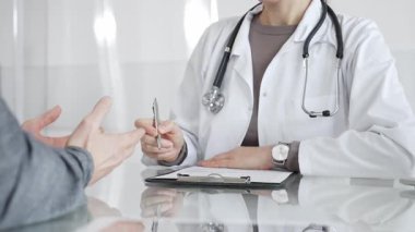 Klinikteki hasta muayenesi sırasında panoya not alan beyaz önlüklü doktor sağlık, teşhis ve bakım kararlarına odaklanmış. İlaç ve sağlık hizmetleri