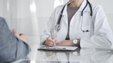 Klinikteki hasta muayenesi sırasında panoya not alan beyaz önlüklü doktor sağlık, teşhis ve bakım kararlarına odaklanmış. İlaç ve sağlık hizmetleri