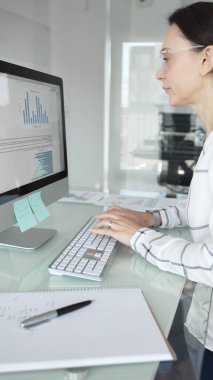 Ofisteki profesyonel kadın klavyede yazı yazıyor, piyasa grafiklerini ve mali verileri iş stratejisi için ekranda analiz ediyor. İş insanları kavramı