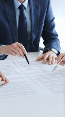 İş adamları ellerinde kalemlerle belgeleri inceliyor ve sözleşme imzalama, hukuki danışma, müzakere ve önemli anlaşma işbirliğini temsil eden bir tartışmaya girişiyorlar.