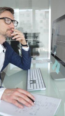 Düşünceli iş adamı stratejik planlamaya odaklanmış, modern ofis ortamında bilgisayar ve evrak işleriyle masa başında notlar yazıyor. İş adamları konsepti