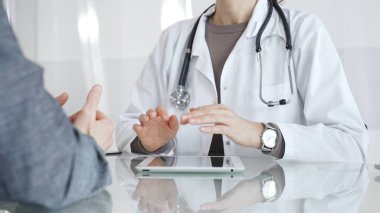 Klinik muayenesi sırasında bir hastaya tıbbi bilgileri açıklarken el hareketi yapan beyaz önlüklü kadın bir doktor. İlaç ve sağlık hizmetleri