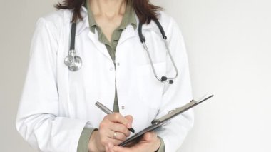 Yeşil bluz üzerine steteskop ve beyaz önlük giyen kimliği belirsiz kadın doktor tıbbi uzmanlığı ve hasta bakımını temsil eden bir panoya yazı yazıyor. İlaç ve sağlık hizmetleri kavramı.