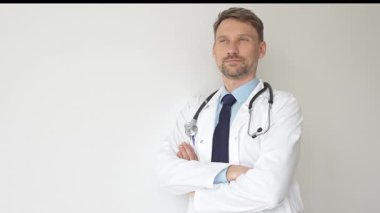 Kendine güvenen erkek doktor kolları çapraz duruyor, steteskop ve beyaz önlük giyiyor. Düşünceli bir şekilde, tıp alanında profesyonelliği ve uzmanlığı somutlaştırıyor. İlaç ve sağlık hizmetleri