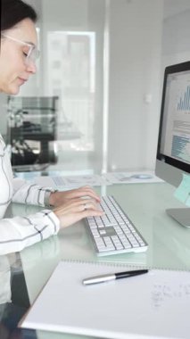 Ofisteki profesyonel kadın klavyede yazı yazıyor, piyasa grafiklerini ve mali verileri iş stratejisi için ekranda analiz ediyor. İş insanları kavramı