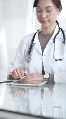 Steteskoplu beyaz önlüklü bir tıp uzmanı dijital sağlık hizmetleri, teletıp ve EMR veri incelemesi ve danışma için bir tablet kullanıyor. İlaç ve sağlık hizmetleri