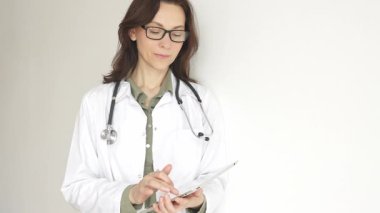 Parlak, modern bir ofiste dijital tablet kullanan profesyonel bir kadın doktor, hasta kayıtlarını ve tıbbi verileri verimli bir şekilde yönetiyor. İlaç ve sağlık hizmetleri