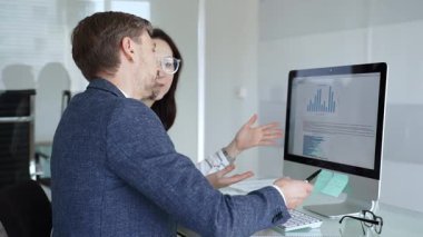 Bilgisayarda birlikte çalışan iki iş arkadaşı ekranda gösterilen grafik ve grafiklere işaret ederek veri analizini tartışıyor. İş insanları kavramı