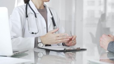 Klinikteki hasta muayenesi sırasında panoya not alan beyaz önlüklü doktor sağlık, teşhis ve bakım kararlarına odaklanmış. İlaç ve sağlık hizmetleri