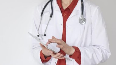 Tuğla kırmızısı bluz ve stetoskop üzerine beyaz önlük giyen kimliği belirsiz profesyonel doktor dijital tablet kullanıyor. Bu da tıpta yenilikçi sağlık uygulamaları olduğunu gösteriyor. Sağlık hizmeti kavramı