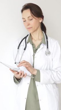 Steteskop takan doktor kadın ve yeşil bluzun üzerine beyaz önlük giymiş hasta bakımını ve tıbbi uzmanlığı temsil eden bir panoya yazı yazıyor. İlaç ve sağlık hizmetleri kavramı.