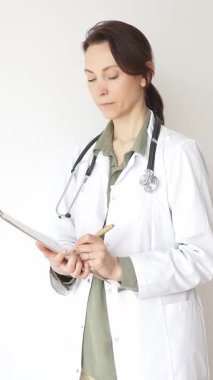 Steteskop takan doktor kadın ve yeşil bluzun üzerine beyaz önlük giymiş hasta bakımını ve tıbbi uzmanlığı temsil eden bir panoya yazı yazıyor. İlaç ve sağlık hizmetleri kavramı.