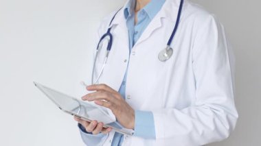 Mavi bluz ve steteskop üzerine beyaz önlük giyen kimliği belirsiz kadın doktor dijital tablet kullanıyor. Bu da tıpta yenilikçi sağlık uygulamaları olduğunu gösteriyor. Sağlık ve Tıp Konsepti.