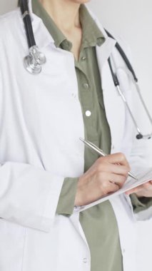 Yeşil bluz üzerine steteskop ve beyaz önlük giyen kimliği belirsiz kadın doktor tıbbi uzmanlığı ve hasta bakımını temsil eden bir panoya yazı yazıyor. İlaç ve sağlık hizmetleri kavramı.