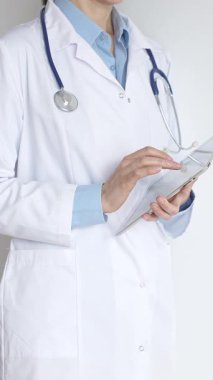 Mavi bluz ve steteskop üzerine beyaz önlük giyen kimliği belirsiz kadın doktor dijital tablet kullanıyor. Bu da tıpta yenilikçi sağlık uygulamaları olduğunu gösteriyor. Sağlık ve Tıp Konsepti.