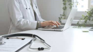 Stetoskop ve tıbbi kayıtlar doktorun karşısındaki masada. Bilgisayarında tıbbi bir büro var. İnternet üzerinden sağlık hizmeti ya da teletıp hizmeti sunuyor. Tıp konsepti.