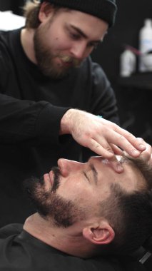 Profesyonel berber müşterilerinin sakallarını ustura ile tıraş eder, jöle sürer ve modern berber ortamında titizlikle bakımı için sıcak havlu kullanır..