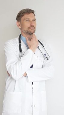 Kendine güvenen erkek doktor kolları çapraz duruyor, steteskop ve beyaz önlük giyiyor. Düşünceli bir şekilde, tıp alanında profesyonelliği ve uzmanlığı somutlaştırıyor. İlaç ve sağlık hizmetleri