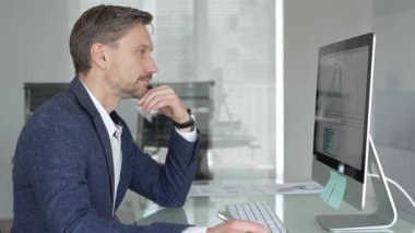 Düşünceli iş adamı stratejik planlamaya odaklanmış, modern ofis ortamında bilgisayar ve evrak işleriyle masa başında notlar yazıyor. İş adamları konsepti