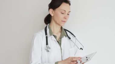 Yeşil bluz ve steteskop üzerine laboratuvar önlüğü giyen kendine güvenen doktor kadın doktor modern sağlık ve tıbbi teknolojiyi temsil eden dijital tablet kullanıyor. Tıp konsepti.