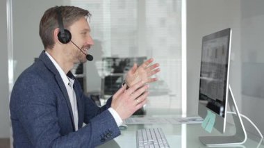 Erkek profesyonel kulaklık takıyor, bilgisayarla iletişim kuruyor, modern ofis ortamında müşteri hizmetleri sağlıyor. İş adamları konsepti