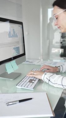 Ofisteki profesyonel kadın klavyede yazı yazıyor, piyasa grafiklerini ve mali verileri iş stratejisi için ekranda analiz ediyor. İş insanları kavramı