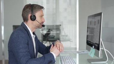 Ofiste kulaklık ve mikrofon takan bir erkek profesyonel bilgisayar masasında sanal müvekkil toplantısı sırasında güven içinde konuşuyor. İş adamları konsepti