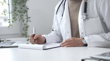 Laboratuvar önlüğü ve steteskop giyen doktor tıbbi reçete yazıyor ya da ofis masasında oturan tıbbi belgeleri dolduruyor. İlaç ve sağlık hizmetleri