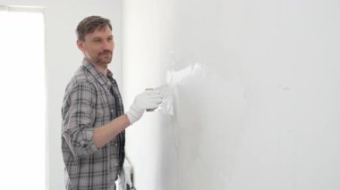 İnşaat işçisi beyaz duvara alçı yayıyor, ev yenileme projesi sırasında koruyucu eldiven takıyor, profesyonel beceri ve odaklanma ile çalışıyor.