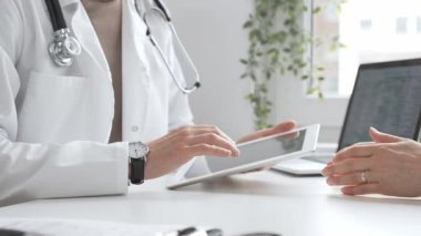 Laboratuvar önlüğü ve steteskop giymiş erkek doktor modern tıp ofisinde tablet kullanırken hastayı dinliyor. İlaç ve sağlık hizmetleri kavramı.