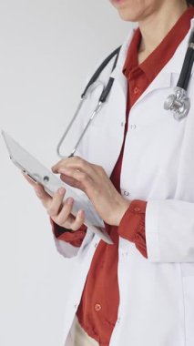 Tuğla kırmızısı bluz ve stetoskop üzerine beyaz önlük giyen kimliği belirsiz profesyonel doktor dijital tablet kullanıyor. Bu da tıpta yenilikçi sağlık uygulamaları olduğunu gösteriyor. Sağlık hizmeti kavramı