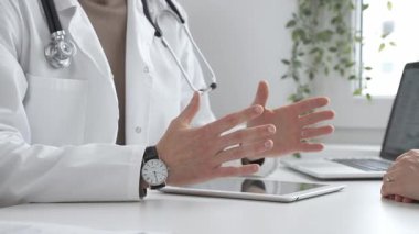 Laboratuvar önlüğü ve steteskop giymiş bir erkek doktor modern tıp ofisinde tablet kullanan hastaya teşhis koymayı açıklarken el kol hareketi yapıyor. İlaç ve sağlık hizmetleri kavramı.