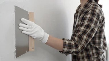 Meçhul kadın inşaat işçisi giyiniyor ve kareli gömlek profesyonel kalitede spatulayla sıva sürüyor. Ev yenileme projesi sırasında ustalıkla yapılmış beyaz duvarı düzleştiriyor..