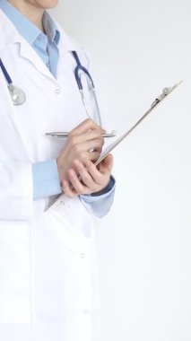 Mavi bluzun üzerine steteskop ve beyaz önlük giyen kimliği belirsiz kadın doktor tıbbi uzmanlığı ve hasta bakımını temsil eden siyah bir panoya yazı yazıyor. Tıp konsepti.