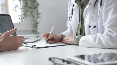 Doktor kadın, erkek hasta sağlığıyla ilgili endişeleri dinliyor ve parlak, modern bir klinikteki muayenede reçete yazıyor. Kapatın. İlaç ve sağlık hizmetleri kavramı.