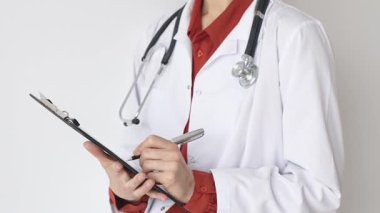 Tuğla kırmızı bluzun üzerine steteskop ve beyaz önlük giyen kimliği belirsiz kadın doktor tıbbi uzmanlığı ve hasta bakımını temsil eden bir panoya yazı yazıyor. İlaç ve sağlık hizmetleri kavramı.