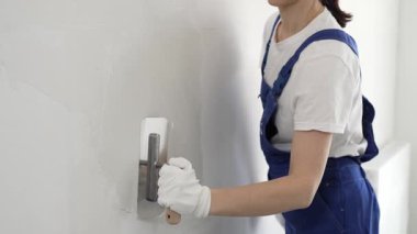 Profesyonel kadın inşaat işçisi, duvarlara alçı yapıştırmak için son malayı kullanıyor. Bu da ev yenileme ve iç dekorasyon konusunda uzman olduğunu gösteriyor..