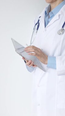 Mavi bluz ve steteskop üzerine beyaz önlük giyen kimliği belirsiz kadın doktor dijital tablet kullanıyor. Bu da tıpta yenilikçi sağlık uygulamaları olduğunu gösteriyor. Sağlık ve Tıp Konsepti.