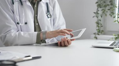 Beyaz laboratuvar önlüğü ve steteskop giyen profesyonel kadın doktor, klinik ortamdaki hasta kayıtlarını incelerken dijital tablet üzerinde çalışıyor. İlaç ve sağlık hizmetleri kavramı