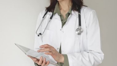 Yeşil bluz ve steteskop üzerine beyaz önlük giyen kimliği belirsiz kadın doktor dijital tablet kullanıyor. Bu da tıpta yenilikçi sağlık uygulamaları olduğunu gösteriyor. Sağlık hizmeti kavramı.