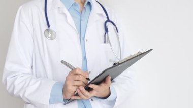 Mavi bluzun üzerine steteskop ve beyaz önlük giyen kimliği belirsiz kadın doktor tıbbi uzmanlığı ve hasta bakımını temsil eden siyah bir panoya yazı yazıyor. Tıp konsepti.