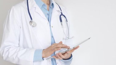 Mavi bluz ve steteskop üzerine beyaz önlük giyen kimliği belirsiz kadın doktor dijital tablet kullanıyor. Bu da tıpta yenilikçi sağlık uygulamaları olduğunu gösteriyor. Sağlık ve Tıp Konsepti.