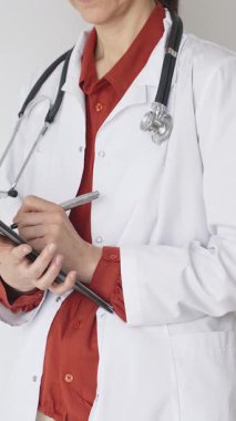 Tuğla kırmızı bluzun üzerine steteskop ve beyaz önlük giyen kimliği belirsiz kadın doktor tıp uzmanlığını ve hasta bakımını temsil eden bir panoya yazı yazıyor. Tıp konsepti.