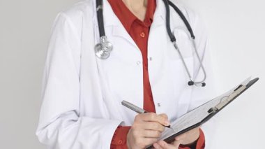 Tuğla kırmızı bluzun üzerine steteskop ve beyaz önlük giyen kimliği belirsiz kadın doktor tıbbi uzmanlığı ve hasta bakımını temsil eden bir panoya yazı yazıyor. İlaç ve sağlık hizmetleri kavramı.