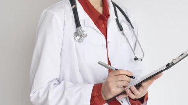 Tuğla kırmızı bluzun üzerine steteskop ve beyaz önlük giyen kimliği belirsiz kadın doktor tıbbi uzmanlığı ve hasta bakımını temsil eden bir panoya yazı yazıyor. İlaç ve sağlık hizmetleri kavramı.