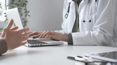 Klinik ortamdaki sağlık hizmetleri sırasında hasta bilgilerini, laptopunu ve steteskopunu kayıt altına alan beyaz önlüklü bir tıbbi uzman. İlaç ve sağlık hizmetleri kavramı